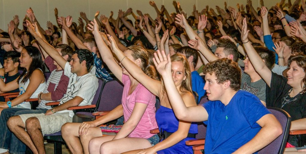 College hypnotist show audience raising hands to volunteer. Stage Hypnotist Erick Känd.